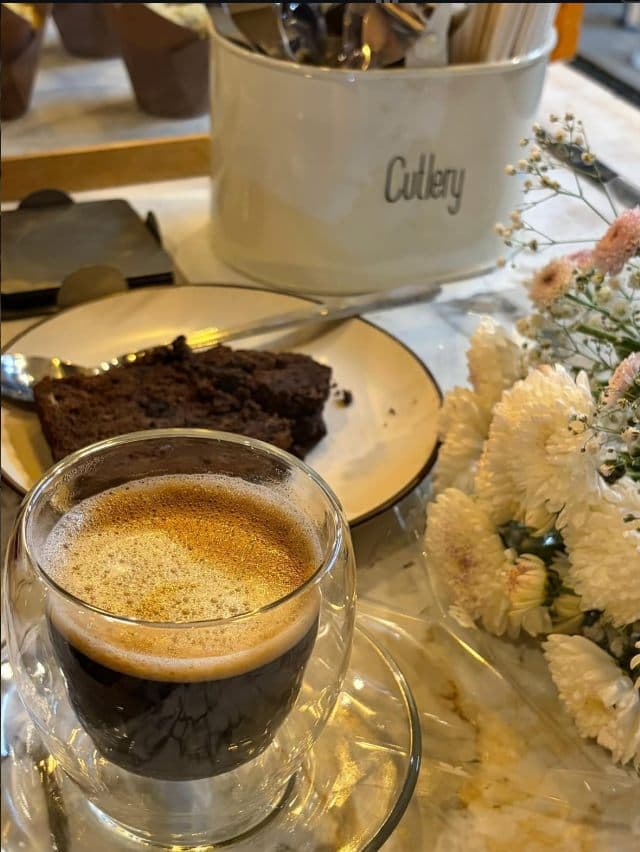 A glass of espresso beside a slice of cake and fresh flowers inside Kaizen.